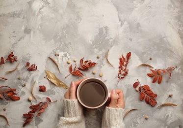 Woman with cup of hot drink at grey table, top view with space for text. Cozy autumn atmosphere