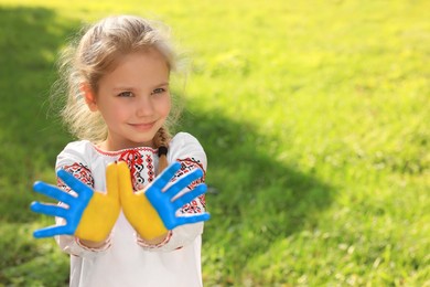 Photo of Little girl with hands painted in Ukrainian flag colors outdoors, space for text. Love Ukraine concept