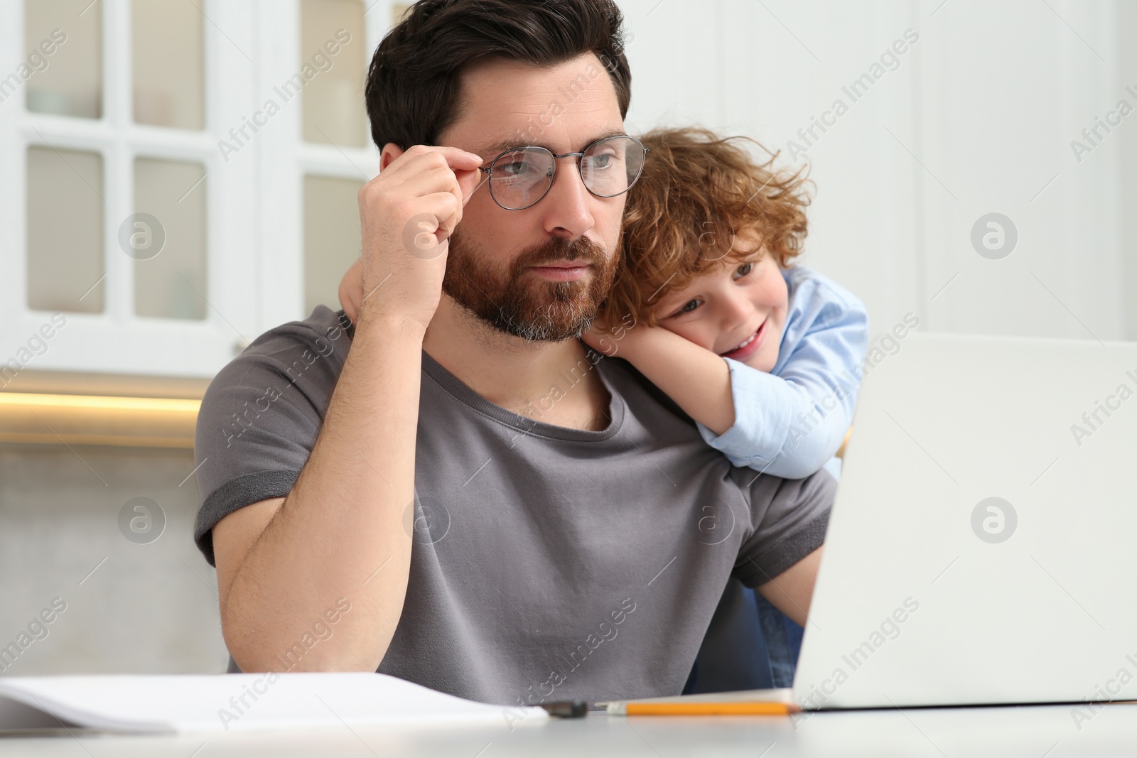 Photo of Man with laptop working remotely at home. Father and son at desk