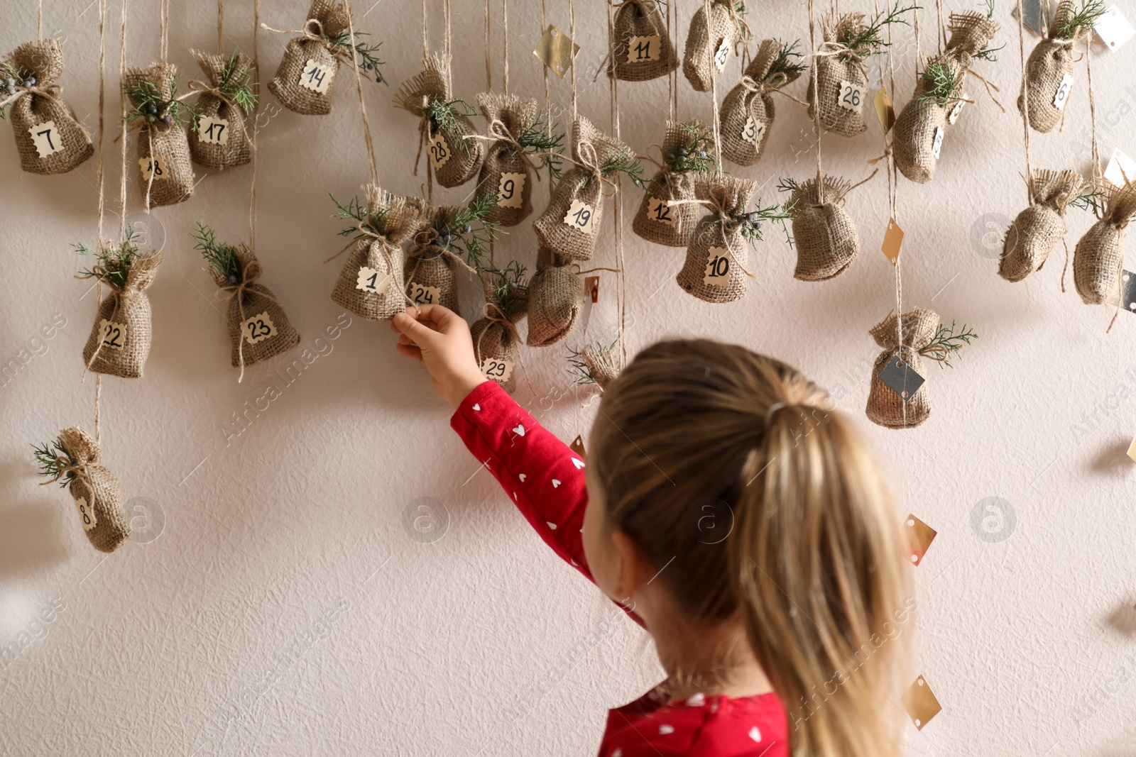 Photo of Little girl taking gift from New Year advent calendar indoors