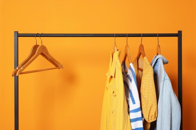 Photo of Rack with stylish clothes on wooden hangers against orange background