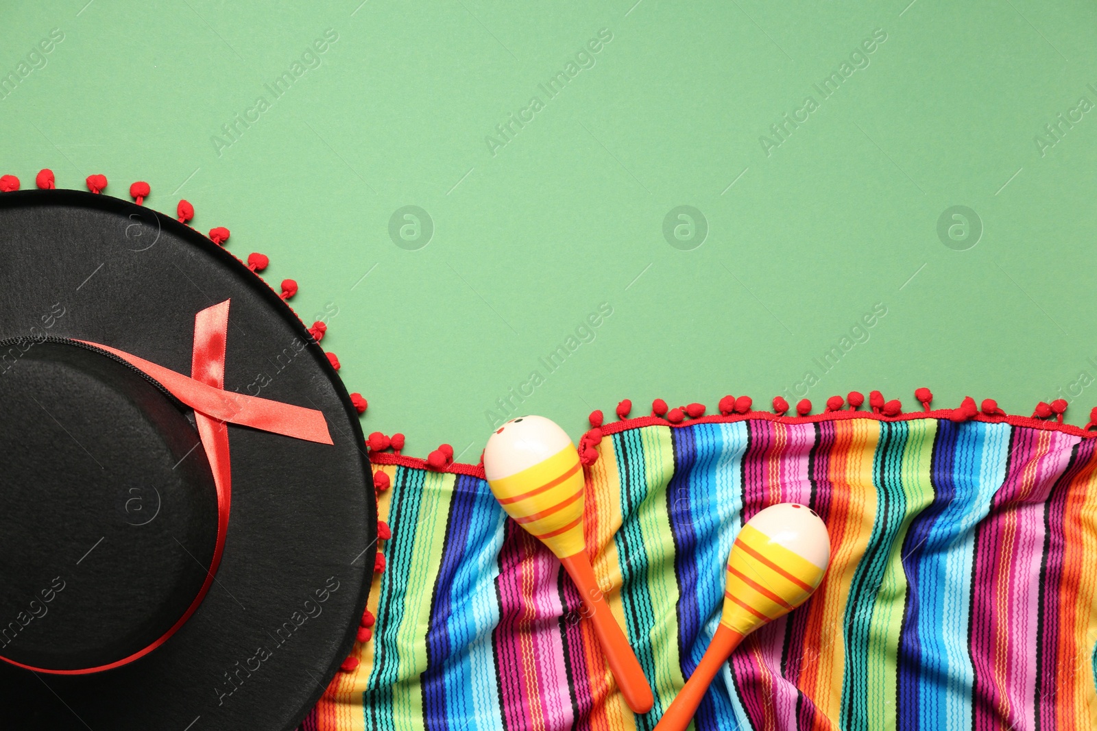 Photo of Mexican sombrero hat, maracas and colorful poncho on green background, flat lay. Space for text