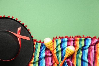 Mexican sombrero hat, maracas and colorful poncho on green background, flat lay. Space for text