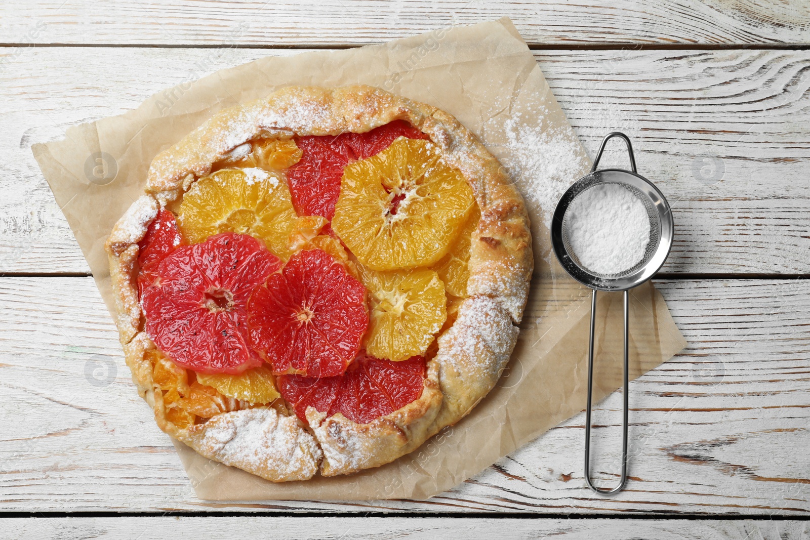 Photo of Delicious galette with citrus fruits and powdered sugar on white wooden table, flat lay