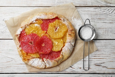 Delicious galette with citrus fruits and powdered sugar on white wooden table, flat lay