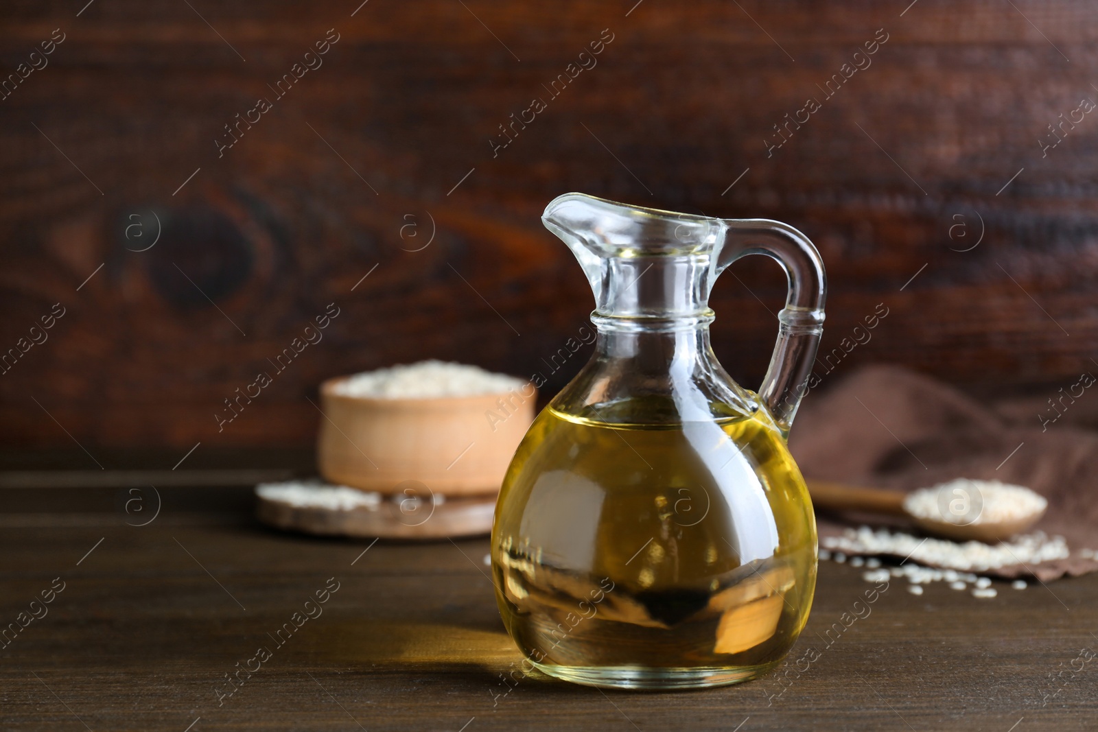 Photo of Jug of organic sesame oil and seeds on wooden table. Space for text