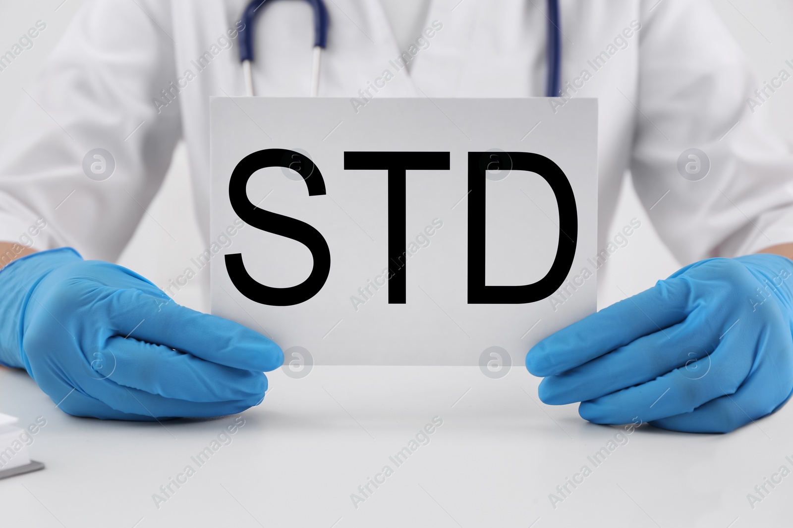 Photo of Doctor holding sheet of paper with abbreviation STD at white table, closeup
