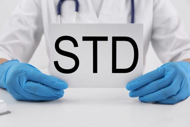 Photo of Doctor holding sheet of paper with abbreviation STD at white table, closeup