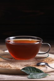 Photo of Aromatic hot tea in glass cup and leaves on wooden table