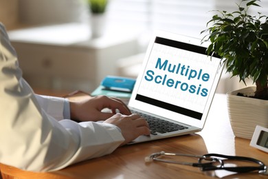 Image of Multiple Sclerosis concept. Doctor working on laptop at wooden table, closeup