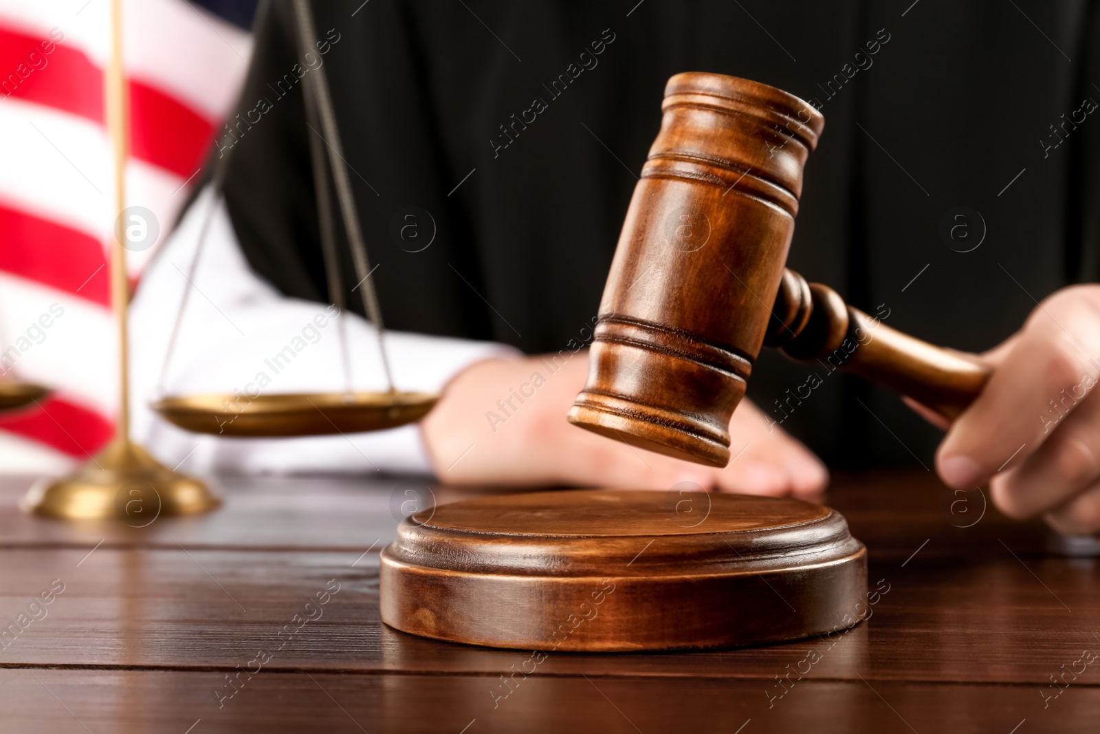 Photo of Judge with gavel at wooden table near American flag, closeup. Space for text