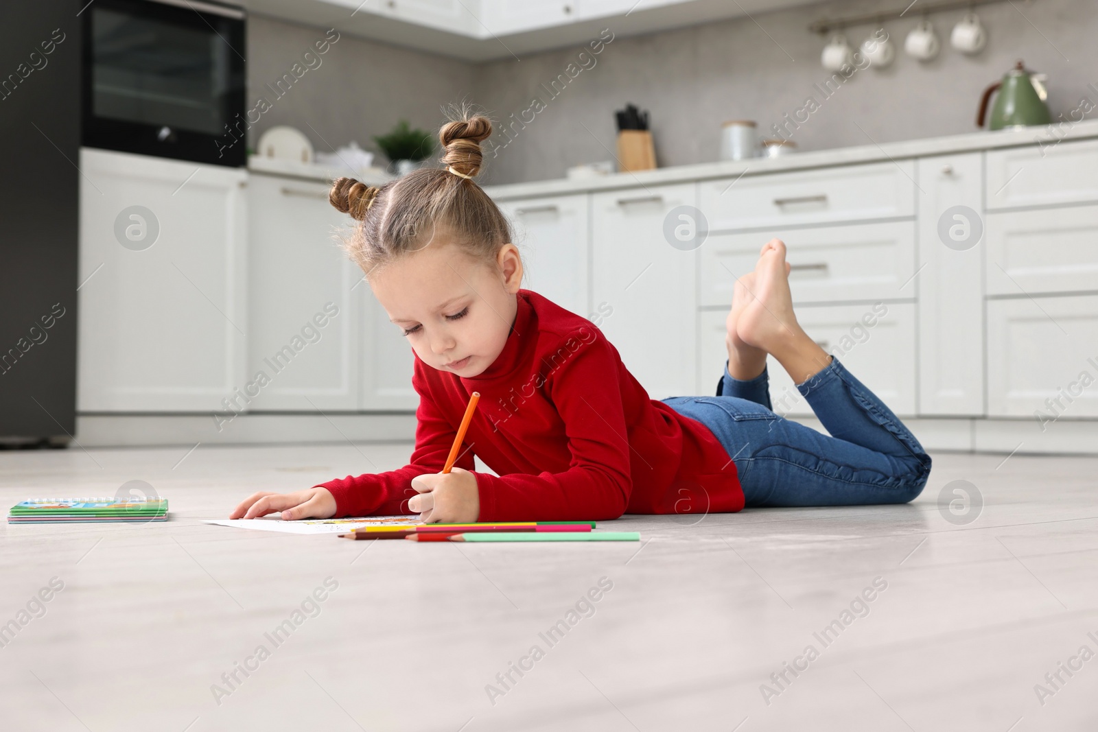 Photo of Cute little girl coloring on warm floor in kitchen. Heating system