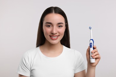 Happy young woman holding electric toothbrush on white background