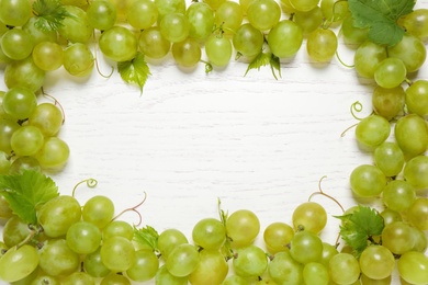 Photo of Frame made with fresh ripe juicy grapes on white wooden table, space for text