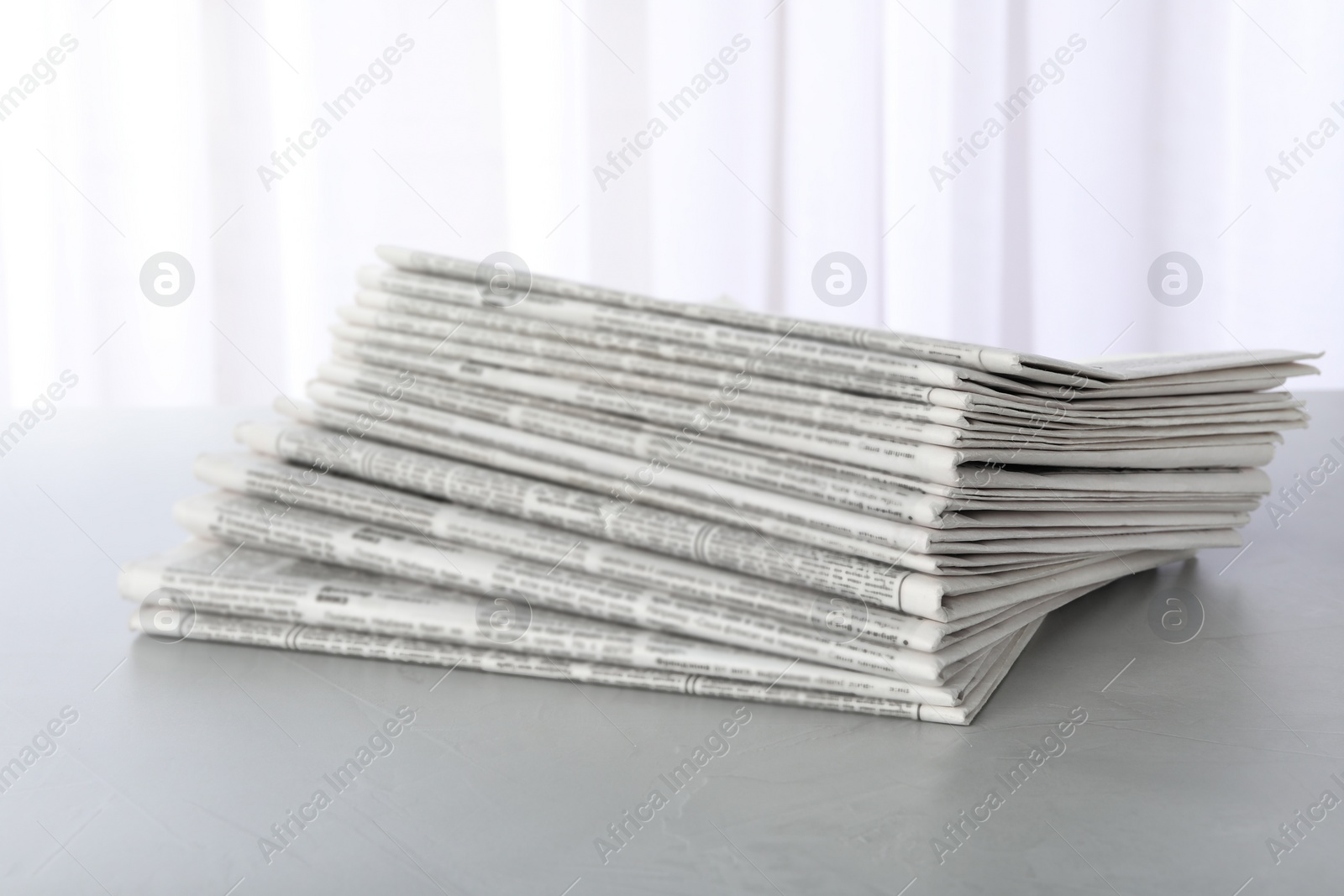 Photo of Stack of newspapers on light grey table. Journalist's work