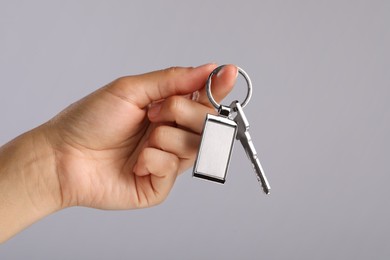 Woman holding key with metallic keychain on grey background, closeup