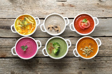 Tasty broth and different cream soups in bowls on old wooden table, flat lay