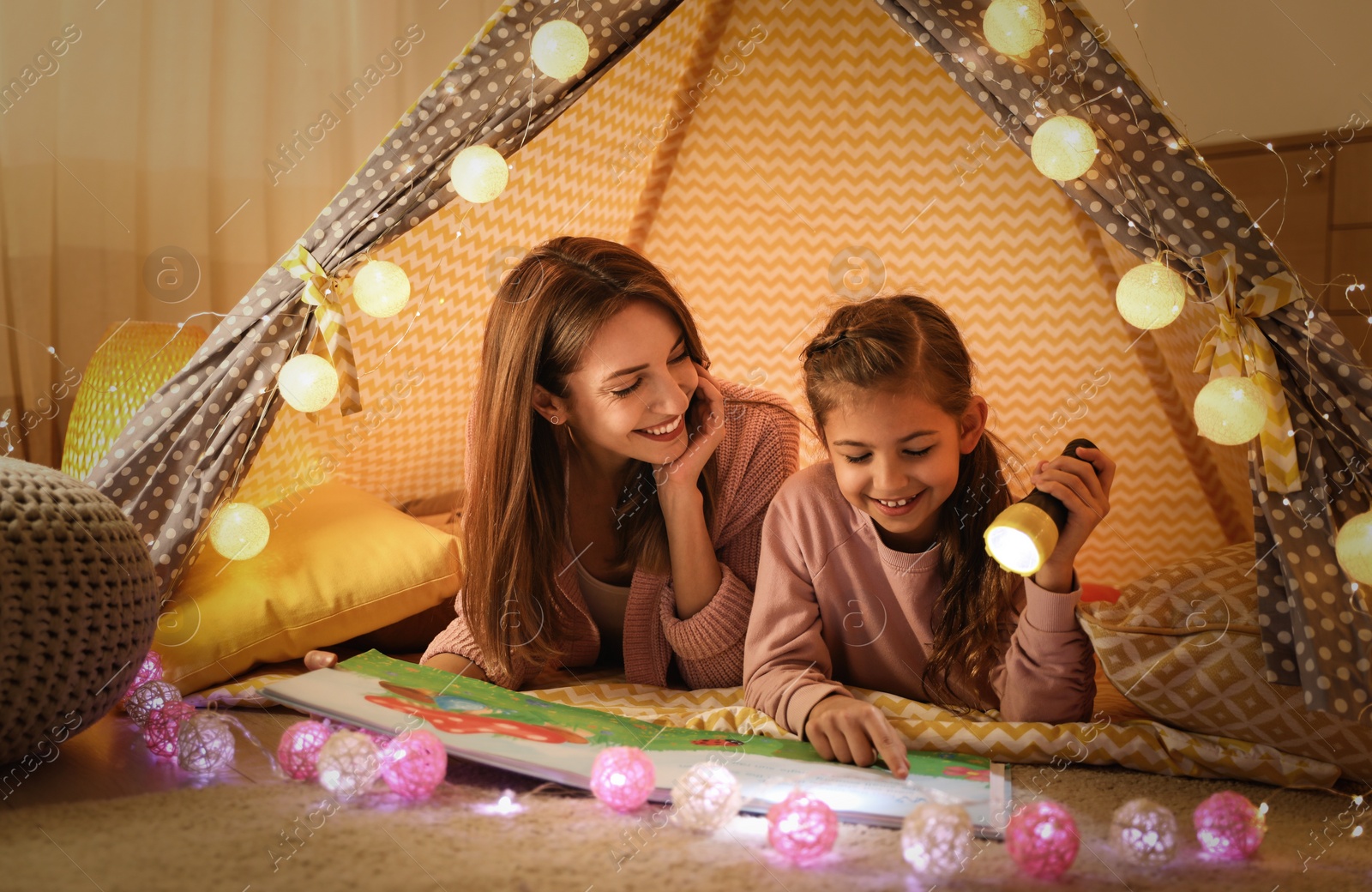 Photo of Mother and daughter with flashlight reading book in play tent