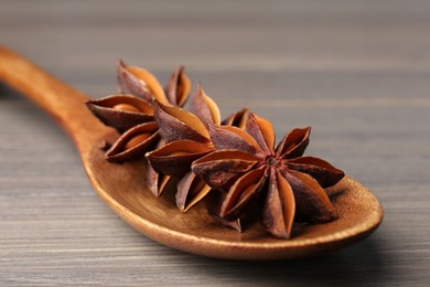 Photo of Spoon with aromatic anise stars on wooden table, closeup