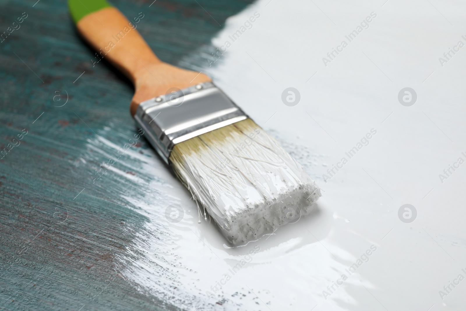 Photo of Brush with white paint on teal wooden background, closeup
