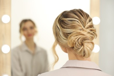 Photo of Woman with beautiful hair style looking at mirror indoors. Space for text