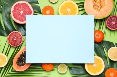 Photo of Different exotic fruits and blank card on green background, flat lay. Space for text