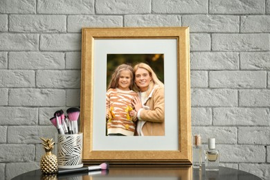 Family portrait of mother and daughter in photo frame on table near white brick wall
