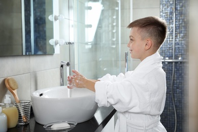 Photo of Little boy washing hands with soap in bathroom