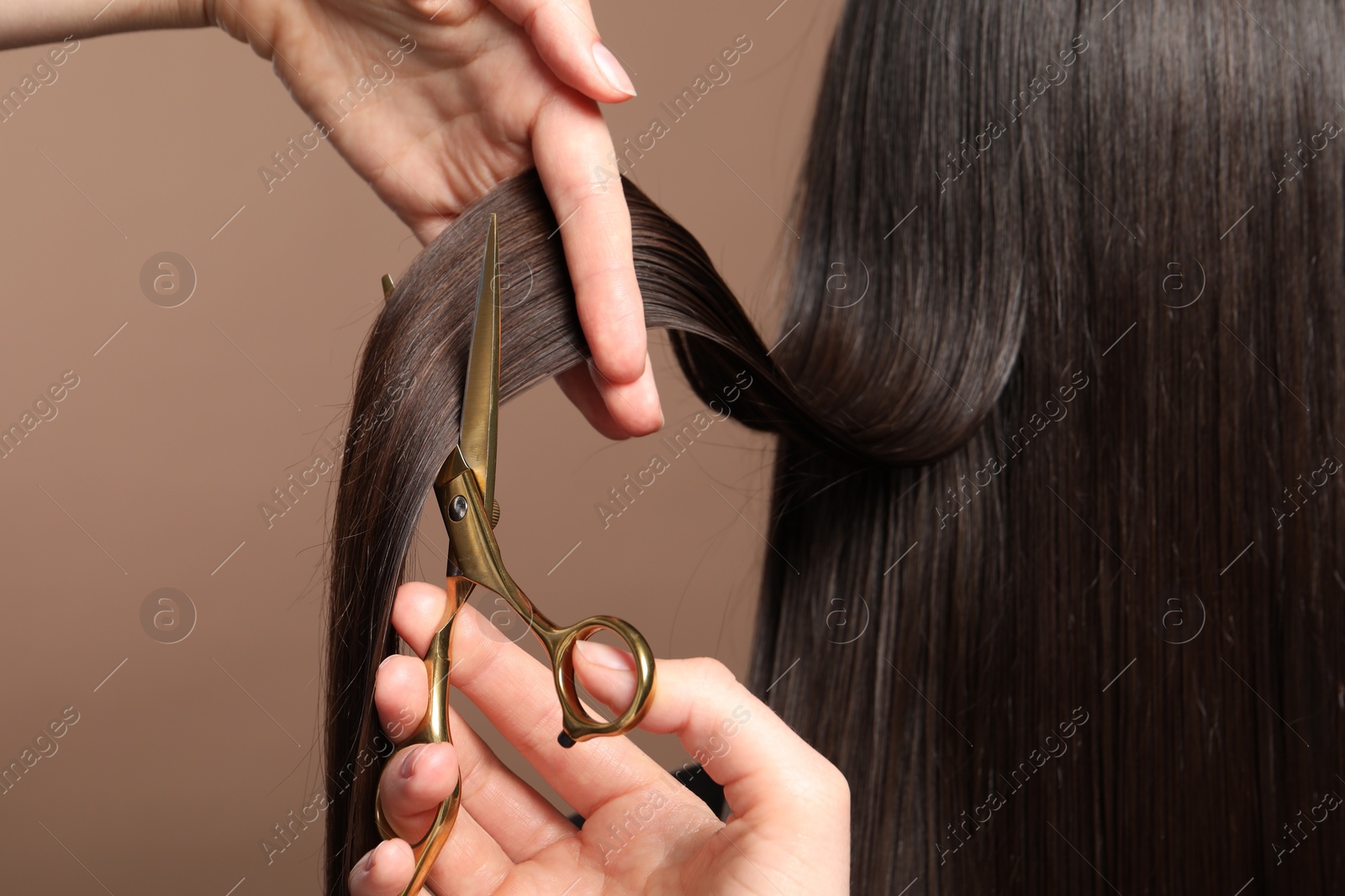 Photo of Hairdresser cutting client's hair with scissors on light brown background, closeup