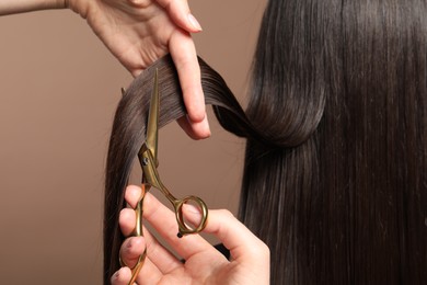 Hairdresser cutting client's hair with scissors on light brown background, closeup