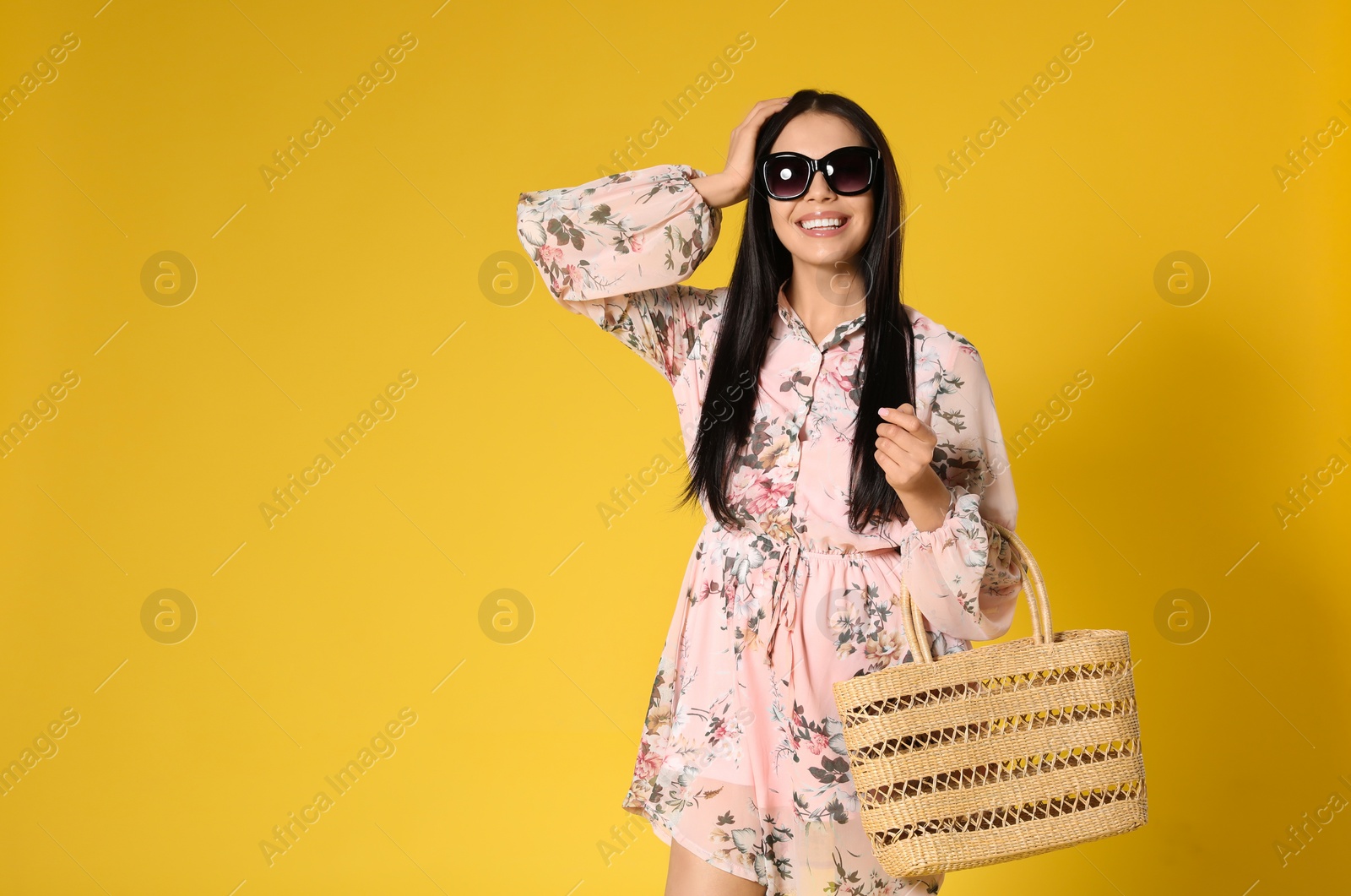 Photo of Young woman wearing floral print dress with straw bag on yellow background