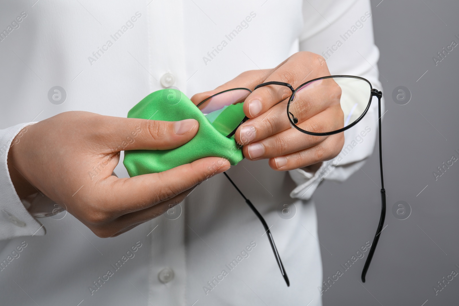 Photo of Woman wiping her glasses with microfiber cloth on grey background, closeup