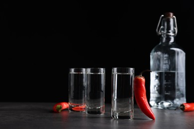 Red hot chili peppers and vodka on grey table against black background, space for text