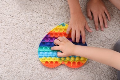 Photo of Little children playing with pop it fidget toy on floor, top view