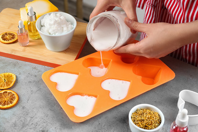 Photo of Woman making natural handmade soap at grey stone table, closeup