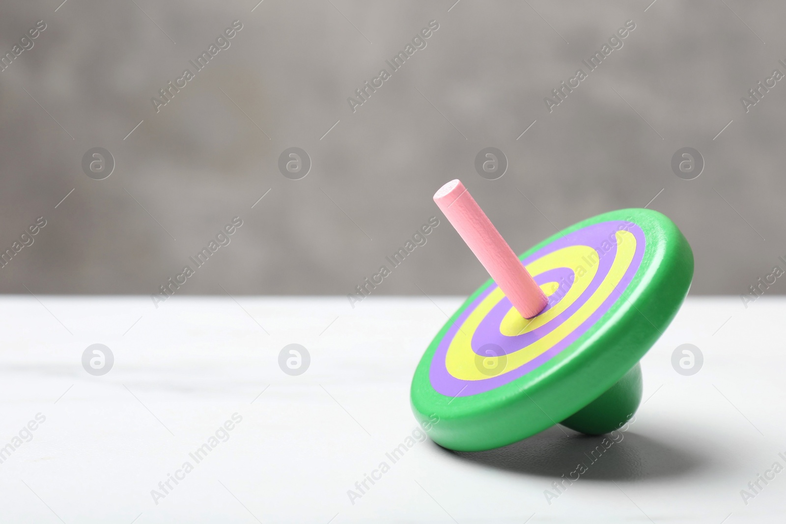 Photo of One bright spinning top on white table, closeup. Space for text