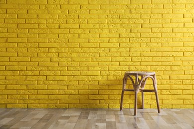 Stylish wooden stool near yellow brick wall, space for text. Interior element