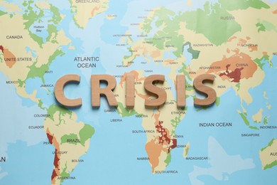 Photo of Word Crisis made of wooden letters on world map, flat lay