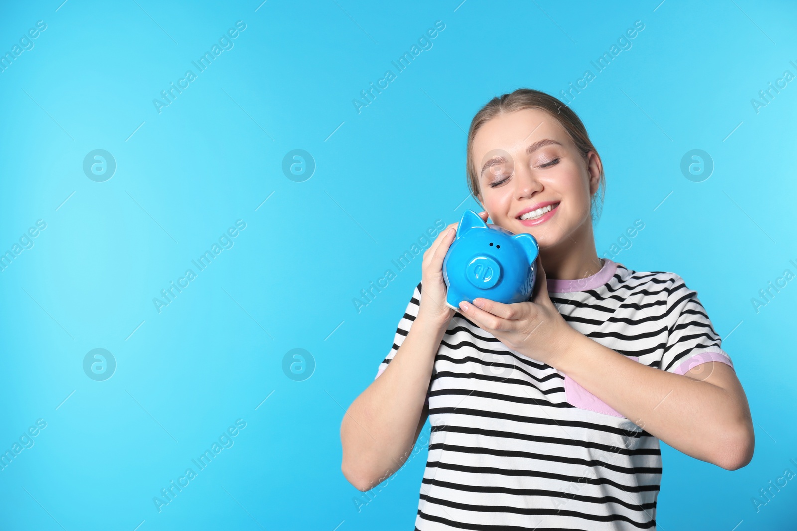 Photo of Happy young woman with piggy bank and space for text on color background. Money saving