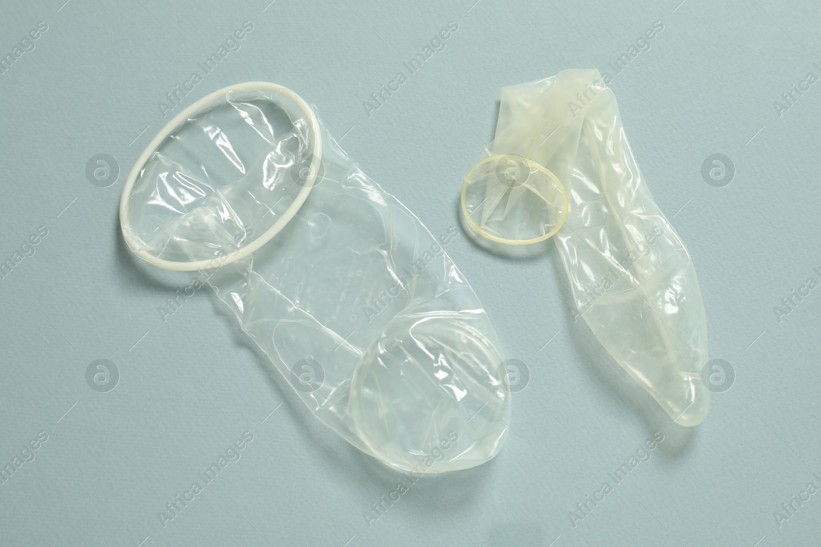 Photo of Unrolled female and male condoms on light blue background, flat lay. Safe sex