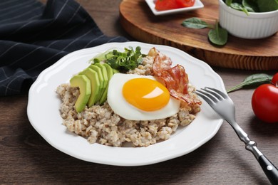 Tasty boiled oatmeal with fried egg, avocado and bacon served on wooden table