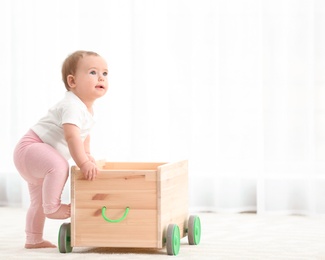 Photo of Cute baby holding on to wooden cart at home. Learning to walk