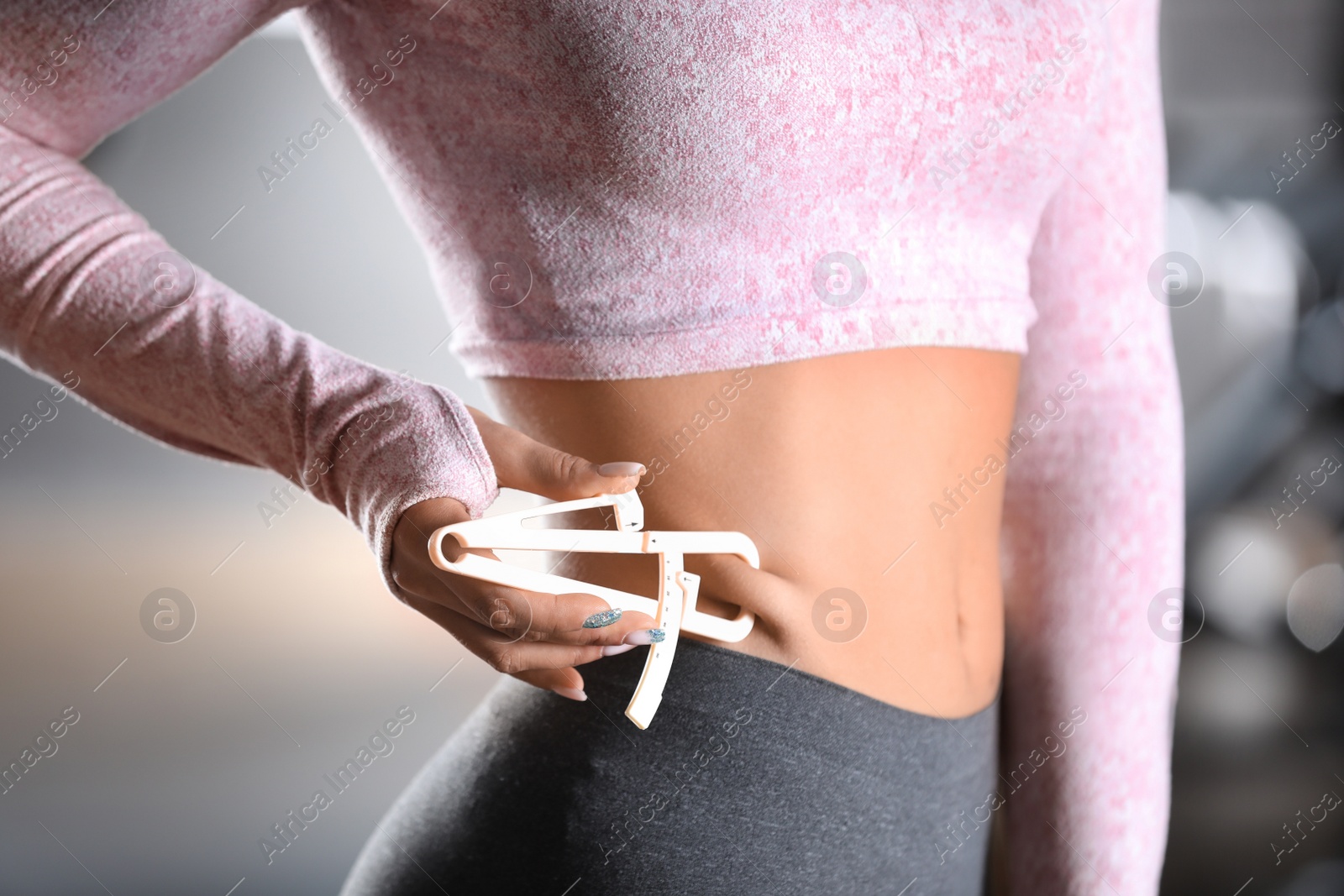 Photo of Woman measuring body fat layer with caliper indoors, closeup