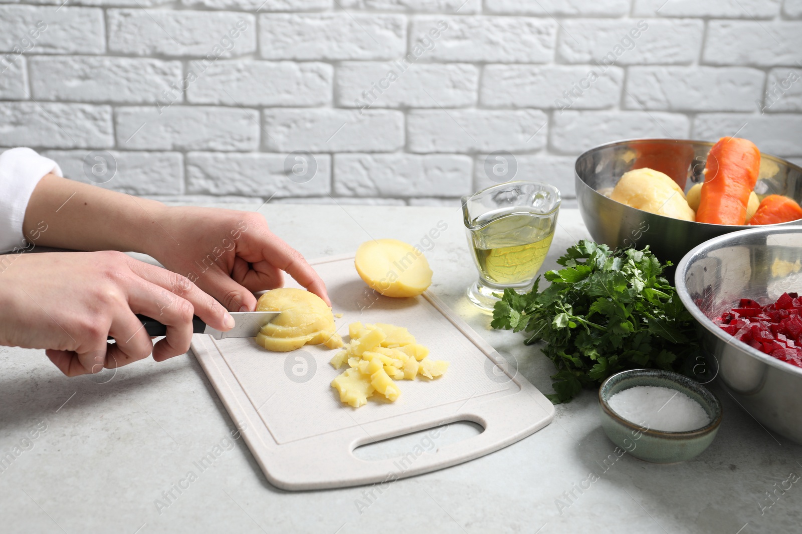 Photo of Woman cutting boiled potatoes at white table, closeup. Cooking vinaigrette salad