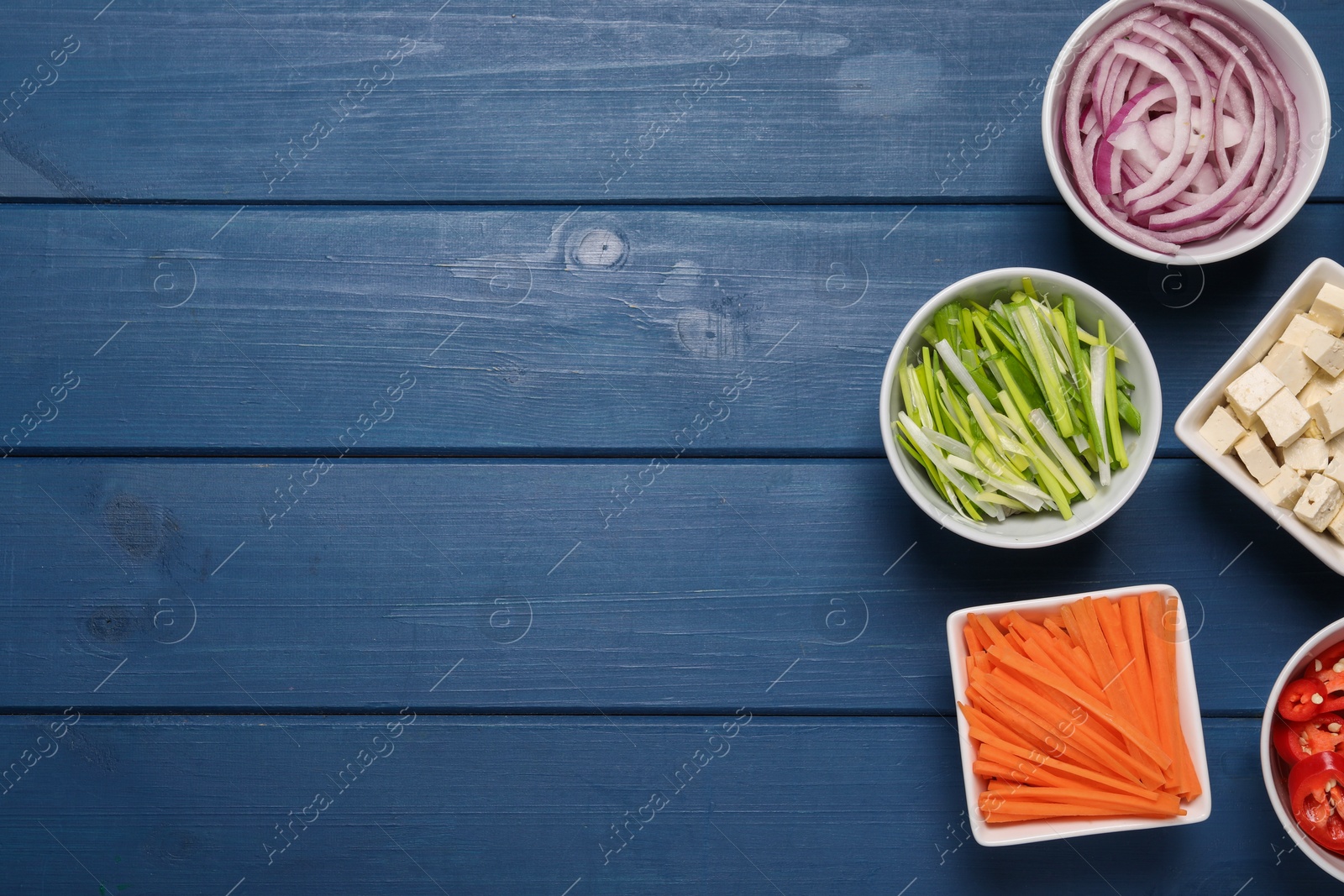 Photo of Cooking delicious ramen soup. Different fresh ingredients in bowls on blue wooden table, flat lay. Space for text