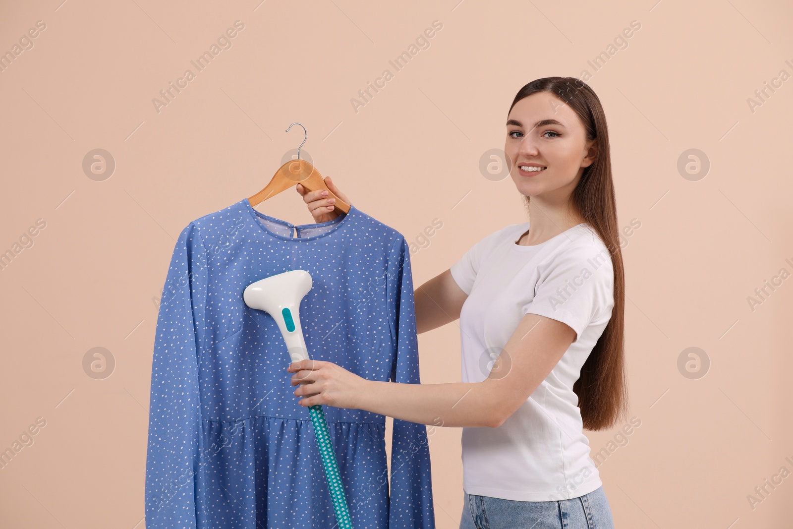 Photo of Woman steaming blouse on hanger against beige background