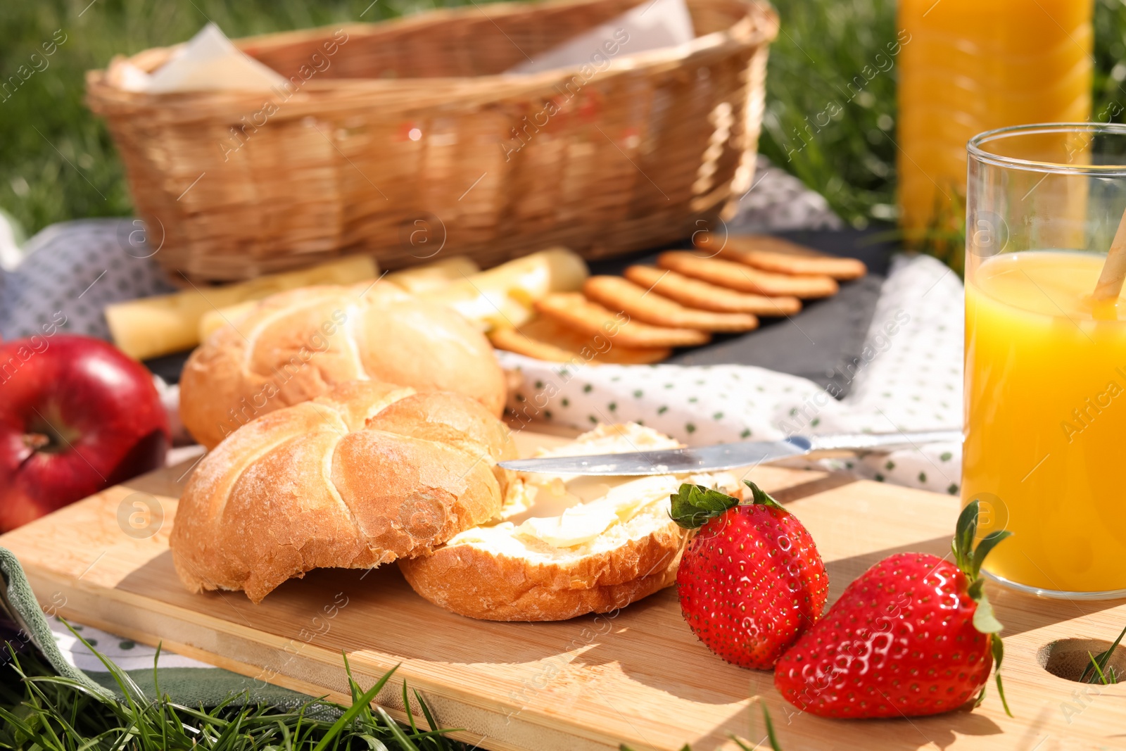 Photo of Blanket with juice and snacks for picnic on green grass, closeup