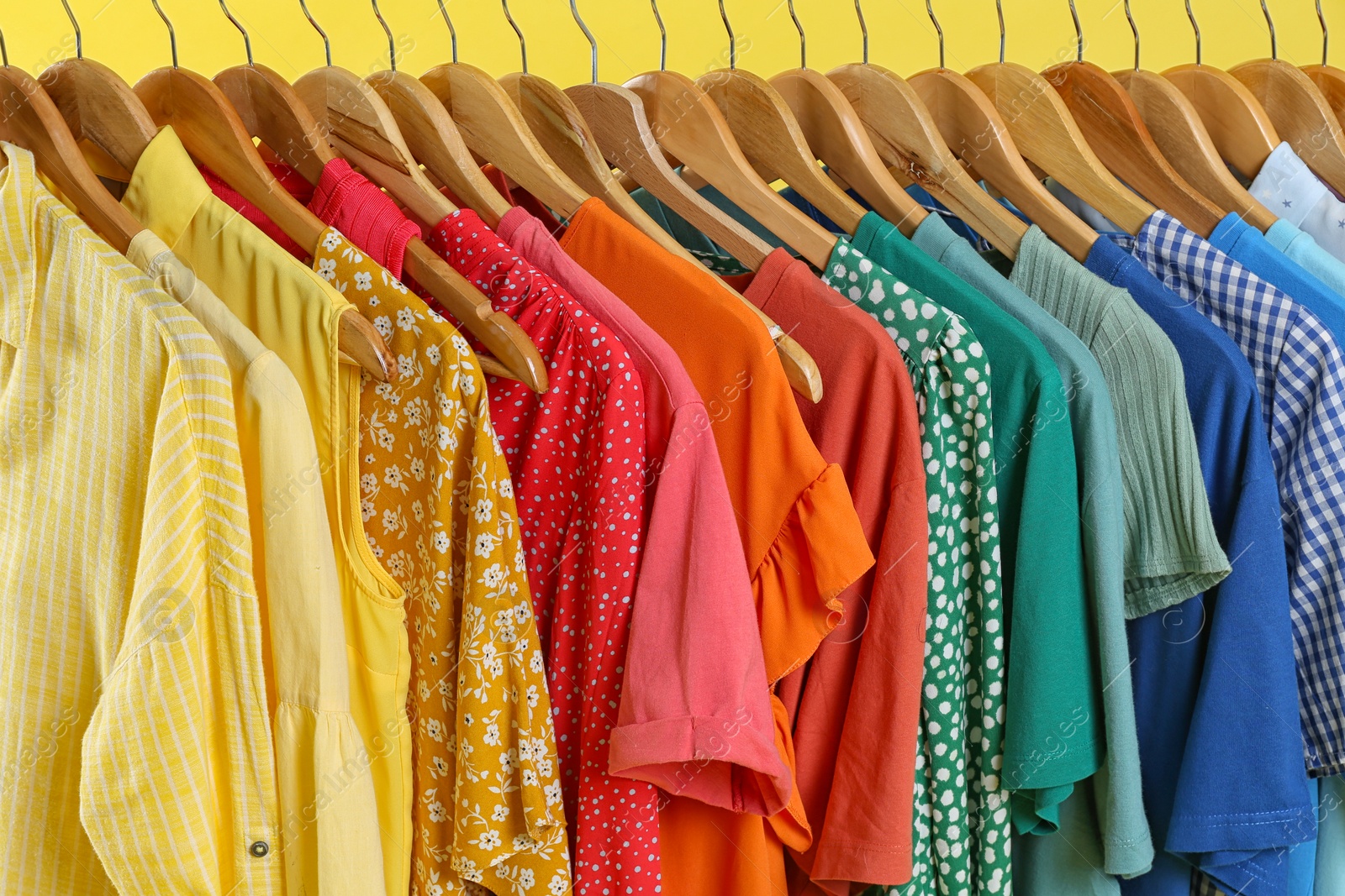 Photo of Bright clothes on hangers against yellow background, closeup. Rainbow colors