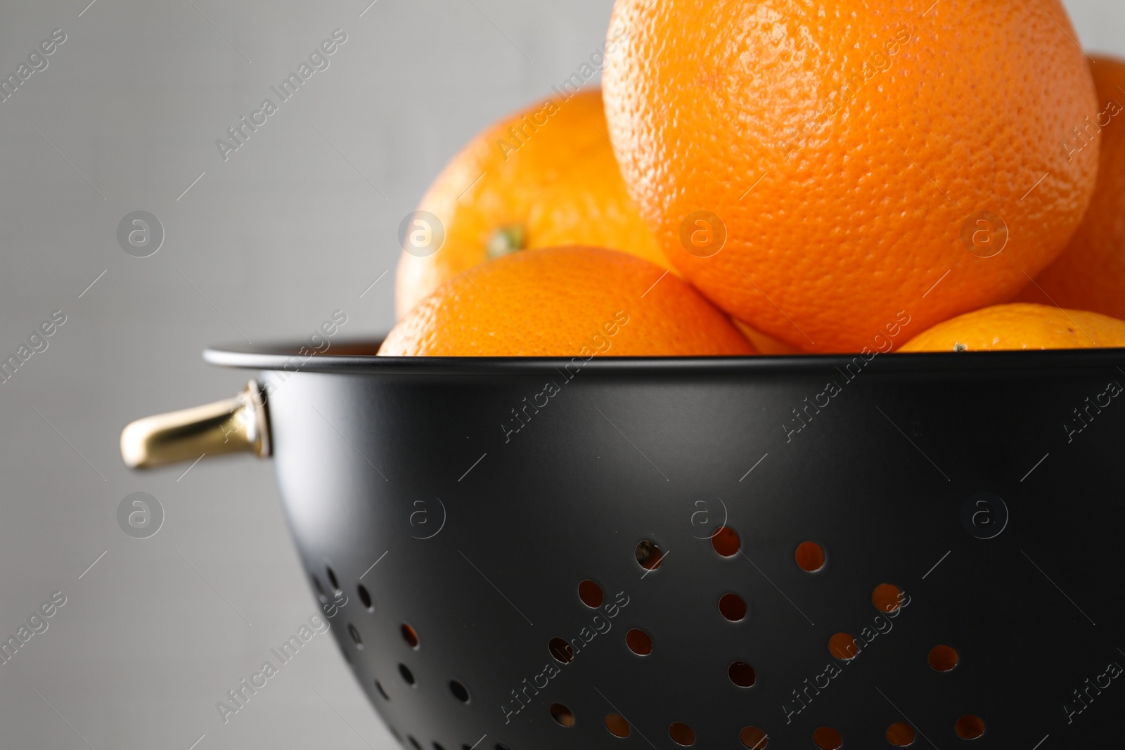 Photo of Fresh ripe oranges in black colander on light background, closeup