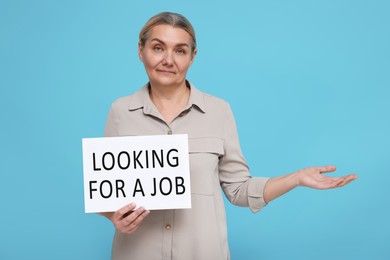 Unemployed senior woman holding cardboard sign with phrase Looking For A Job on turquoise background